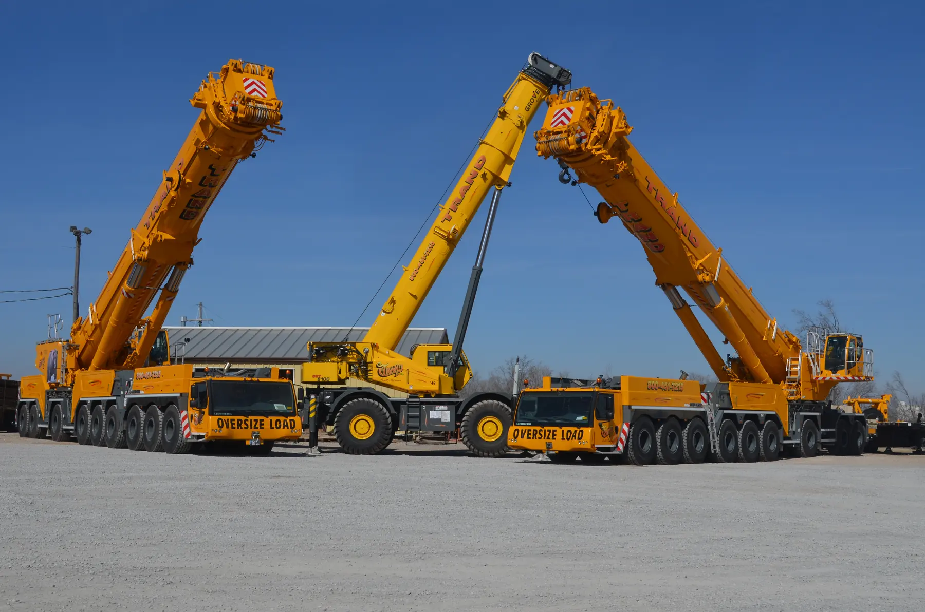 Three Trand Liebherr all-terrain cranes with booms raised in the yard